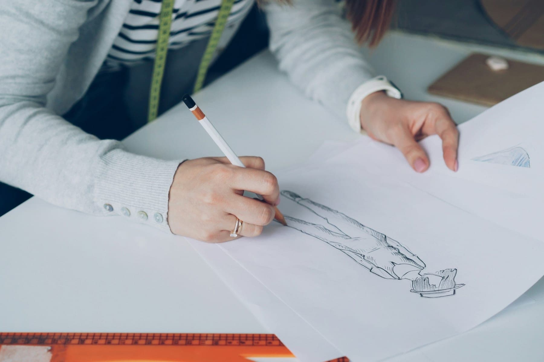 A designer sketching a garment on paper beside a ruler and a tape measure