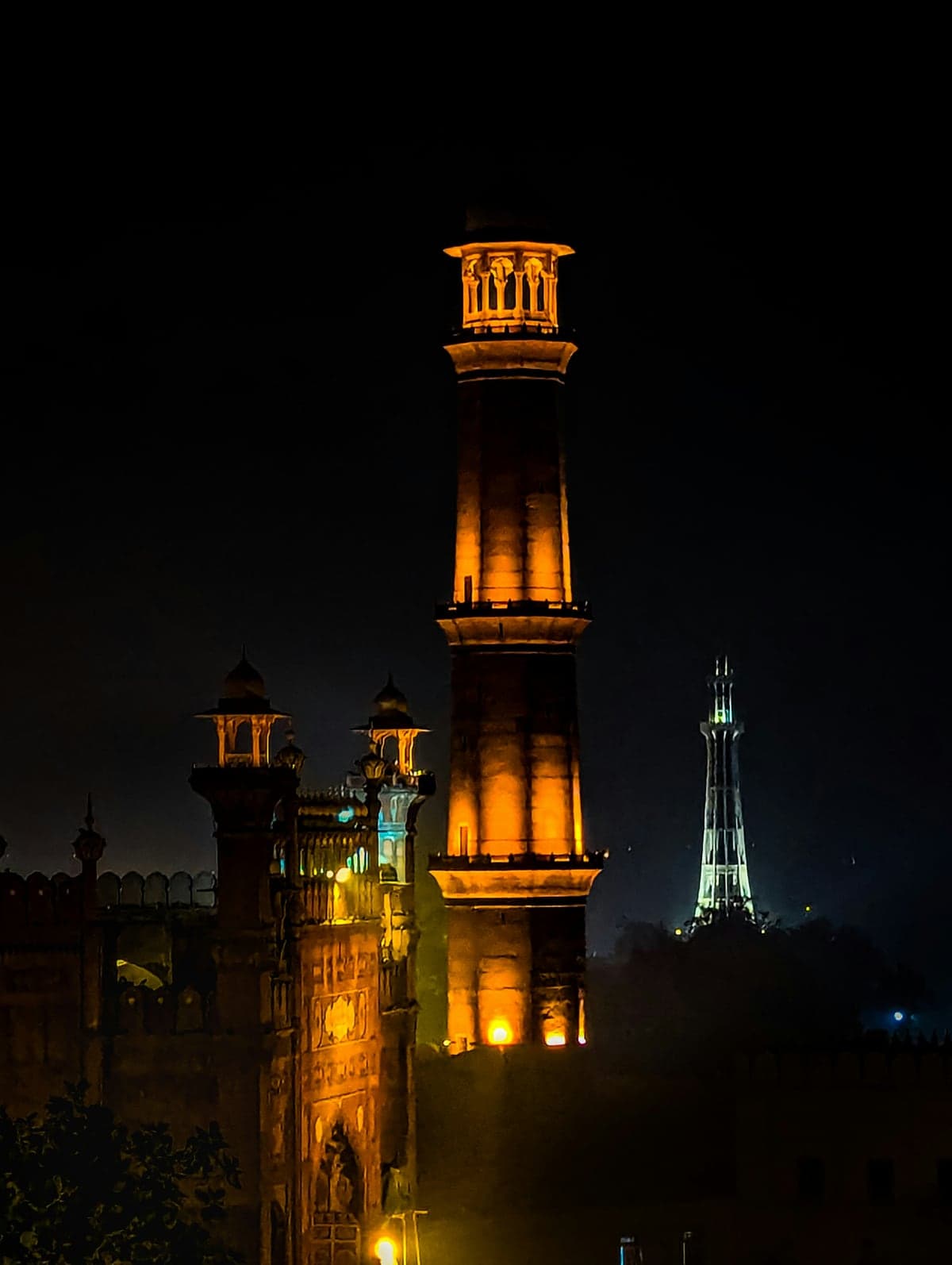 Lahore at night: a lit minaret of the Badshahi Mosque, with the Minar e Pakistan beyond