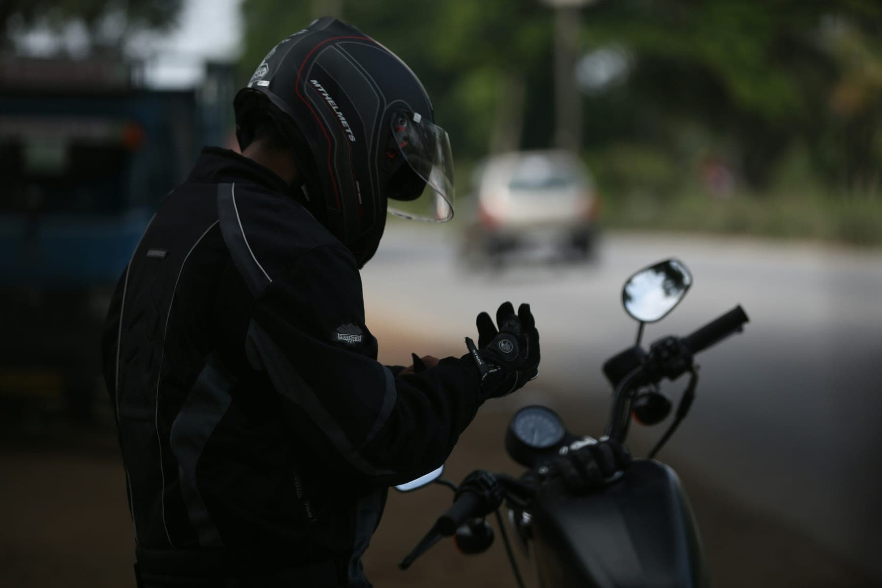 A rider in a riding jacket putting on gloves beside a motorcycle