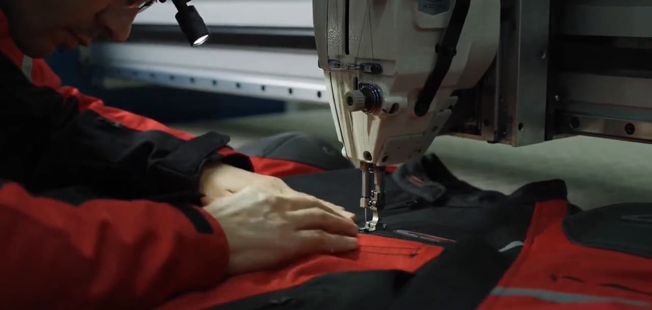 An operator guiding a red and black jacket under a sewing machine needle